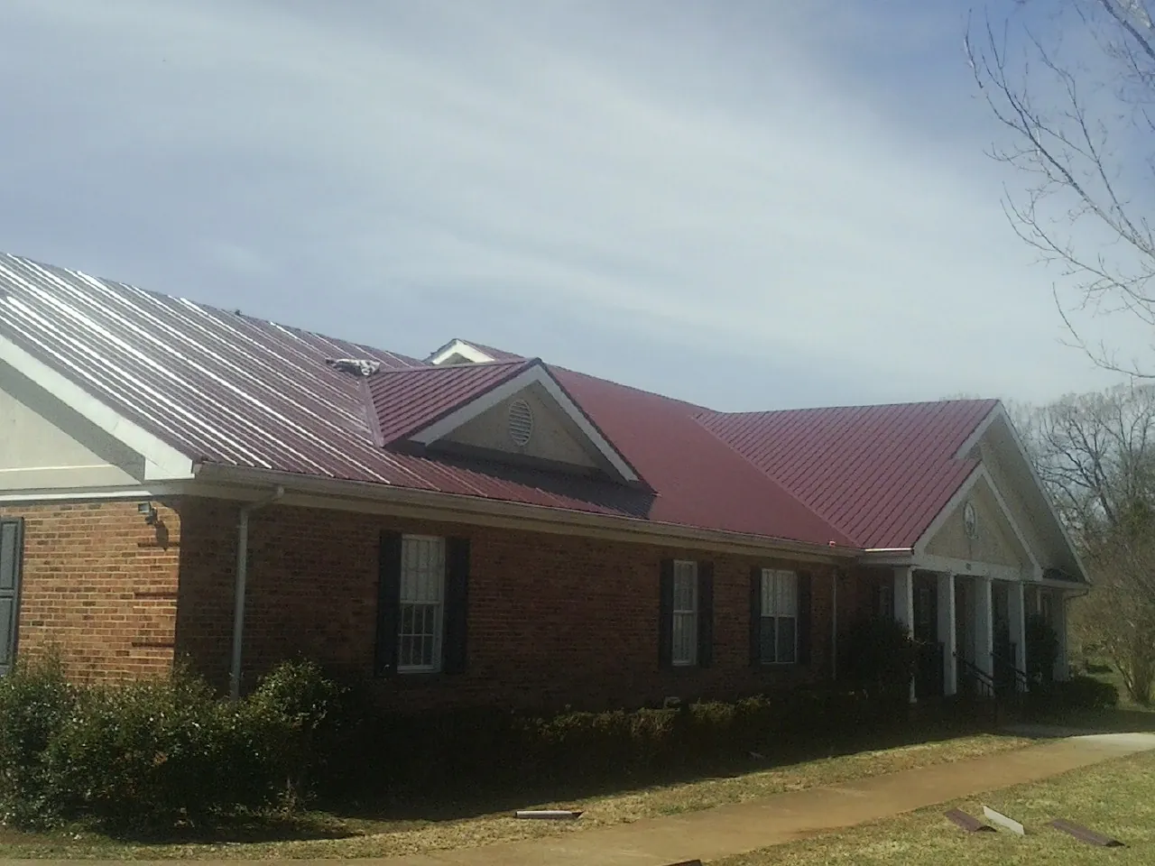 Red metal roof with gabled entries on a long brick building, from a Hail Damage Roof Repair job in Ottawa