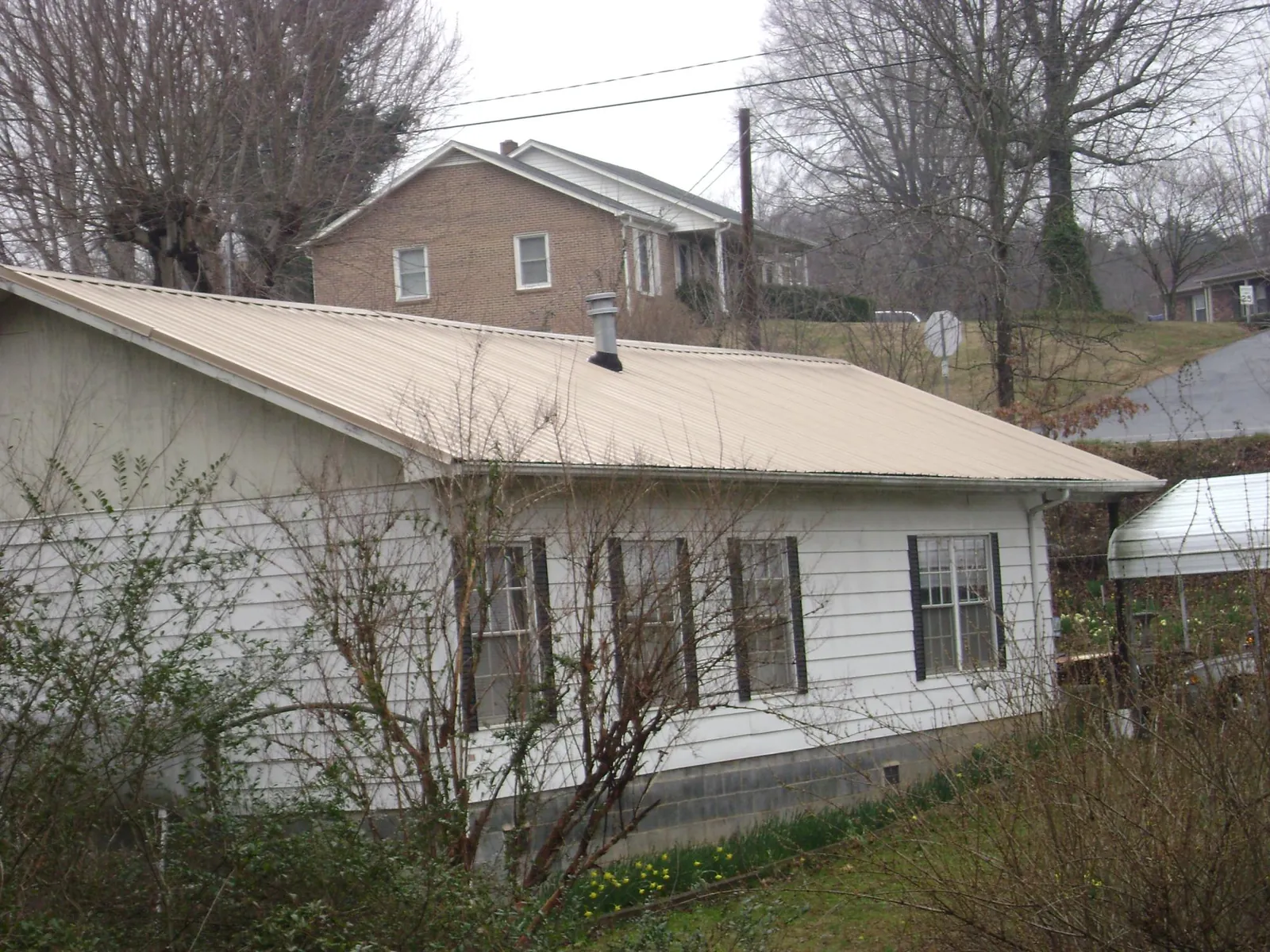 Tan metal roof on a white sided house set into a hillside — Commercial Roofing by Roofing Brothers in Ottawa